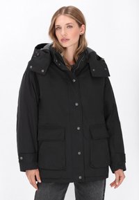 Sort parka-jakke med hætte, der har trykknapper, store forlommer og et glat, mat stof. Grå foring synlig ved hætten.