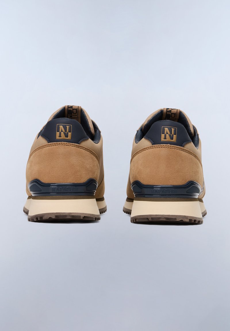 Zapatillas de ante marrón con acentos en azul marino, que destacan por su diseño curvado, refuerzo en el talón y suela de goma texturizada. Logo dorado en la parte trasera.