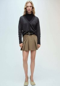 Cardigan gri închis cu decolteu în V și închidere cu nasture, asortat cu o fustă plisată khaki și pantofi bej cu toc; texte netede, design ajustat.