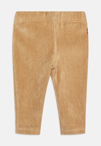 Corduroy pants in light tan, featuring vertical ribbing, a stretchy waistband, and a small brand tag on the side. Soft texture.