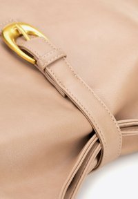 Borsa in pelle beige con tracolla annodata, caratterizzata da una fibbia color oro. Texture liscia con dettagli di cucitura che accentuano il design.