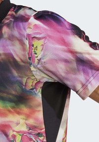 Maglietta a maniche corte con un design astratto colorato che presenta tonalità di rosa, viola e verde; un accento nero sul lato per il contrasto.