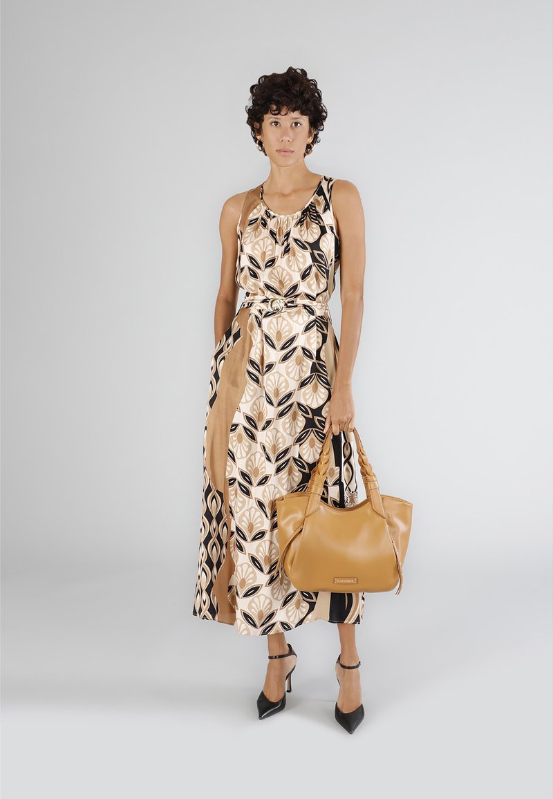 Ärmlös maxiklänning i beige med svart och brun lövmönster; tillsammans med en tan-färgad handväska och svarta högklackade skor. Slät tygfinish.