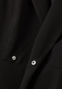 Tessuto nero con una texture liscia, caratterizzato da bottoni argentati e cuciture precise lungo le cuciture.