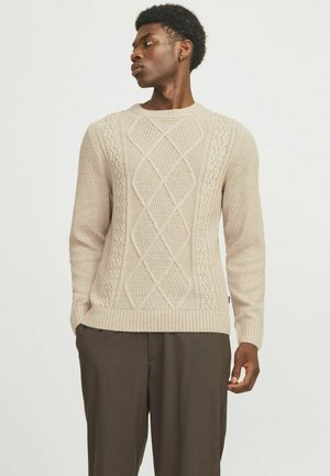 Suéter de punto beige con patrones texturizados, incluyendo diseños trenzados y de diamante, con puños y dobladillo acanalados.