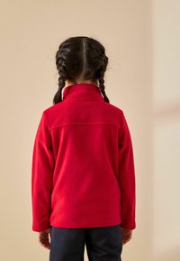 Czerwony polarowy sweter z wysokim kołnierzem i długimi rękawami. Gładka tekstura z przeszyciem z tyłu, zestawiony z ciemnymi spodniami.