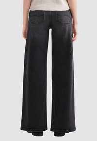 Zwarte wijde jeans met een hoge taille, met twee achterzakken en zichtbare stiksels, getoond vanuit de achteraanzicht.