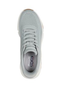 Zapatilla slip-on de color gris claro con parte superior de malla, puntera redonda, cordones elásticos y logo sutil en la plantilla acolchada. Suela de goma con fondo texturizado.