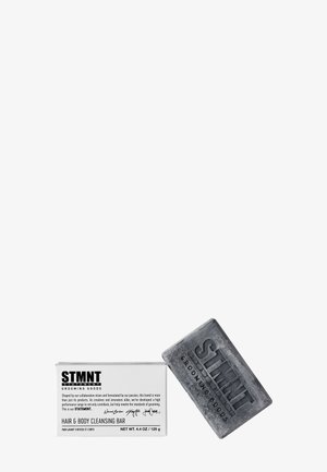 Graue rechteckige Haar- und Körperreinigungsseife mit eingeprägtem "STMNT"-Logo, begleitet von einer weißen Box mit schwarzem Text und Details.