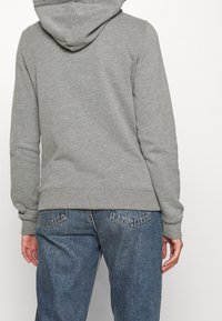 Grå huvtröja med ribbade mudd och nederkant, tillverkad av en bomullsblandning. Tillsammans med löst sittande, blå denimjeans med bakfickor.