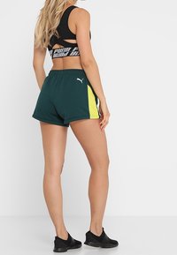 Pantalones cortos deportivos verdes con un panel lateral amarillo, hechos de una tela ligera, con una cintura elástica y un pequeño logo en el muslo.