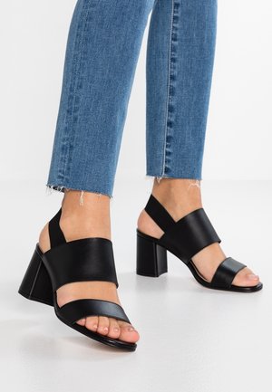 Czarne sandały na obcasie z odkrytymi palcami i dwoma szerokimi paskami. Wykonane z gładkiego materiału. Gruby blokowy obcas, gumowa podeszwa oraz elastyczny pasek na kostkę.
