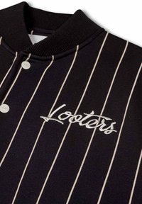 Camisa de jersey a rayas negras con cuello abotonado, que presenta un logo bordado de "Looters" en blanco. Textura suave y diseño ajustado.