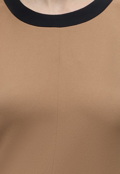 Gros plan d'un haut marron avec un col rond noir montrant la texture du tissu et le détail de la couture centrale.