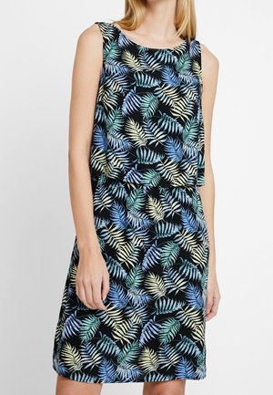 Ärmelloses schwarzes Kleid mit lockerem Überwurf und mehrfarbigem blau-grün-beigem tropischem Blattmuster, getragen von einer stehenden Person.