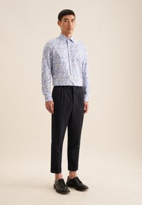 Blauw en wit geprint langemouw shirt, zwarte op maat gemaakte broek en zwarte schoenen. Het shirt heeft een button-down kraag en een slim fit ontwerp.