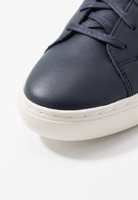 Námořnické kožené tenisky s hladkým povrchem, bílou gumovou podrážkou a odpovídajícími tkaničkami. Disponují minimalistickým designem a jemnými detaily šití.