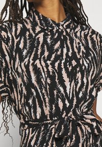 Robe courte à manches courtes noire et rose avec un col, une taille cintrée par un lien et un motif en zigzag audacieux avec des accents blancs.