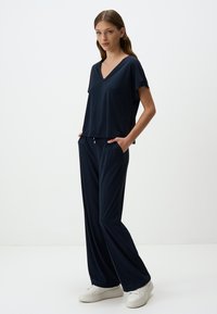 Haut bleu marine à manches courtes et décolleté en V associé à un pantalon ample assorti. Tissu doux et léger avec des poches latérales et une coupe décontractée.