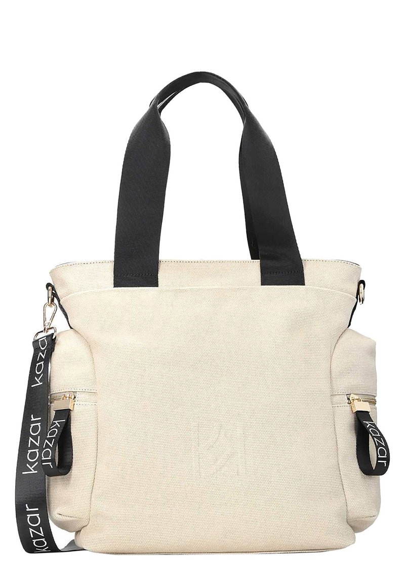 Beżowa torba płócienna z czarnymi paskami i akcentami, z zamykanymi kieszeniami po bokach oraz wytłoczonym logo marki z przodu.
