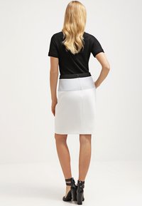 Bílá tužková sukně s kontrastním světle šedým pasem. Hladká textura, přiléhavý střih a zadní zip jako akcent. Černý top s krátkým rukávem.
