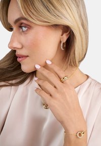 Guldsmycken med intrikata mönster: hoopörhängen med stenar, lager-på-lager ringar och ett armband som har sammanflätade former; släta texturer.