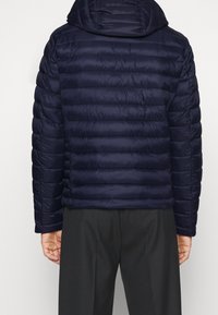 Marinblå puffjacka med huva, med quiltade sektioner och elastiska muddarna, tillverkad av ett smidigt och lätt material.