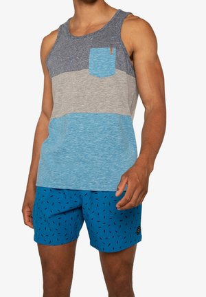 Homme portant un débardeur sans manches à blocs de couleurs avec une poche poitrine et un short de bain bleu orné de petits motifs noirs.