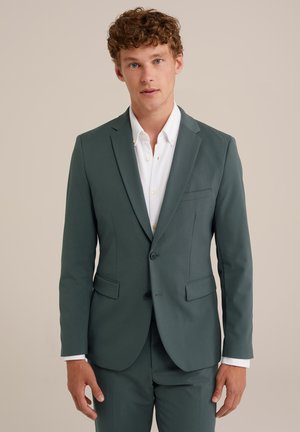 Traje de hombre en tela verde azulado, chaqueta de un solo botón con dos botones, solapas con muesca, dos bolsillos frontales y camisa blanca texturada debajo.