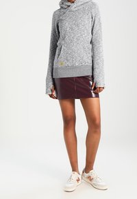 Grå, texturerad hoodie med en framficka och huva med dragsko. Matchad med en glänsande bourgogny mini kjol och vita sneakers med orangea detaljer.