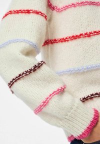 Pull en tricot crème avec des rayures horizontales rouges, roses, bleues et marron. Présente des poignets côtelés et des détails de couture colorés.