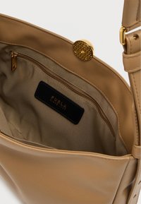 Τσάντα χειρός από δέρμα σε ταμπά απόχρωση με ομαλή υφή, διαθέτει τσέπη με φερμουάρ και κούμπωμα με χρυσό κλιπ. Το εσωτερικό έχει υφασμάτινη επένδυση και ετικέτα με το λογότυπο.