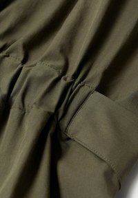 Olivgrüner Stoff mit geraffter Textur, der genähte Nähte und eine glatte Oberfläche aufweist. Enthält ein seitliches Taschendetail.