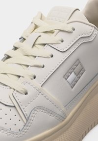 Gros plan d'une basket blanche avec des lacets crème, un embout perforé et le logo Tommy Jeans sur le panneau latéral et la languette.