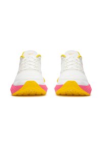 Fehér sportcipők, texturált felsőrésszel, sárga kiegészítőkkel és színes rózsaszín és sárga talppal. A fűzők a fűzőlyukakon át vannak fűzve.