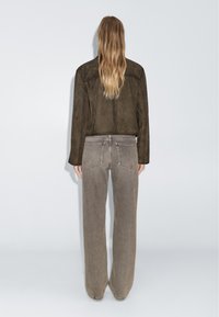 Giacca cropped in camoscio marrone abbinata a jeans beige a vestibilità larga, con tasche posteriori e una finitura in tessuto strutturato.