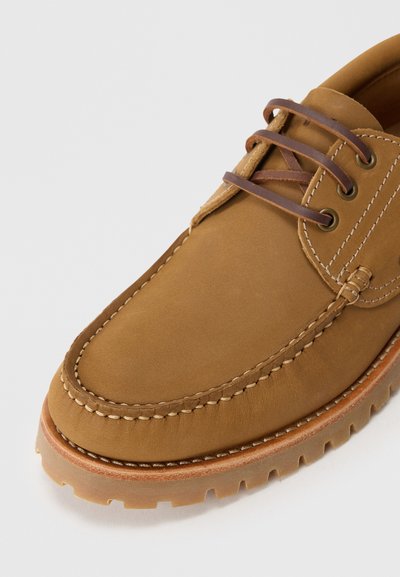 Scarpa da barca in pelle marrone con punta arrotondata, cuciture a contrasto e suola in gomma. Presenta lacci in pelle e occhielli in metallo.