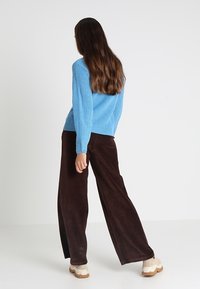 Vaaleansininen neulottu villapaita, jossa on ribbineulos, yhdistetty tummanruskeisiin leveälahkeisiin corduroshousuihin ja kermanvärisiin korotettuihin tennareihin.