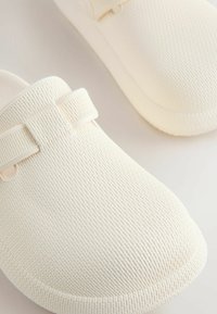 Witte instapschoenen met een gestructureerde mesh buitenkant, voorzien van twee verstelbare bandjes en een afgeronde neus. Zacht, lichtgewicht materiaal.
