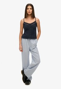 Marineblå knap-down camisole med et tekstureret mønster, parret med lyseblå og hvide stribede bredbenede bukser. Sorte chunky sko fuldender outfittet.