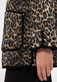 Překládaná bunda v béžovém a černém leopardím vzoru. Disponuje velkou kapsou a černými lemy, zapínání na patentky. Měkká, lesklá textura.