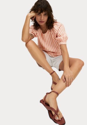 Pruhovaná korálová a bílá blůza s balónovými rukávy, spárovaná se světle šedými šortkami a hnědými páskovými plochými sandály na opálených nohách.