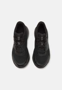 Chaussures de sport noires avec tige en maille, superpositions texturées, design à lacets et semelle en caoutchouc. Présente des éléments de marque sur la languette et sur le côté.