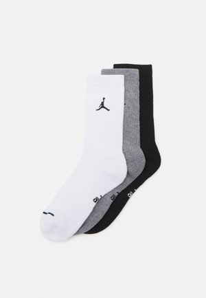 Trīs kokvilnas sporta zeķu pāri baltā, pelēkā un melnā krāsā. Katram ir ribota tekstūra un melnais Air Jordan logo.