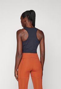 Mustapohja kilpailuhihnalla tank top, jossa on tiukka muotoilu, yhdistettynä korkeavyötäröisiin, saumattomiin oransseihin legginsseihin, jotka sisältävät sileän tekstuurin ja ompeluyksityiskohtia.