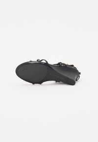 Sandale à talons noirs avec des fines lanières, semelle en caoutchouc texturé et logo embossé sur le côté. Présente un design élégant et minimaliste.