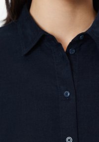 Ciemnoniebieska koszula z kołnierzykiem wykonana z teksturowanej tkaniny, z zapięciem na guziki z przodu oraz małym, subtelnym wzorem na kołnierzu i guzikach.