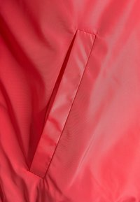 Close-up del bolsillo de una chaqueta de tela coral con costuras limpias y ligeras arrugas en la tela.