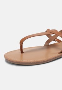 Vaaleanruskeat nahkasandaalit, joissa on varvastuki, ristikkäiset hihnat ja litteä pohja. Reunassa on huomaamaton ommel siistin lopputuloksen saavuttamiseksi.