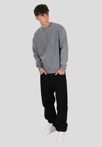 Gray sweatshirt with a crew neckline, paired with loose-fitting black pants. Model wears white sneakers. Smooth fabric, relaxed fit.